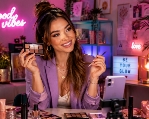 Influencerka prezentuje paletę cieni przed kamerą w kolorowym studiu beauty pełnym kosmetyków do makijażu